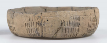 210/A/ML/4 - Pokrywka w formie niewysokiej niemal cylindrycznej miseczki z niewyodrębnionym lekko wklęsłym dnem, ścianki łukowate, nieco rozchylone ku górze o ścienionej, wąskie, zaokrąglonej krawędzi. Cała powierzchnia zewnętrzna ornamentowana: ścianki oraz częściowo górną powierzchnię zdobi 9 dość równomiernie rozmieszczonych na obwodzie grup odcisków prostokątnego stempelka (po 6-7 rzędów składających się z 6-9 pionowych odcisków), pod wylewem pozioma linia sznurowa (nakładająca się na ornament stempelkowy), mniej więcej pośrodku dna 2 koncentryczne, nieregularne koła odciśnięte sznurem wokół większego z nich 