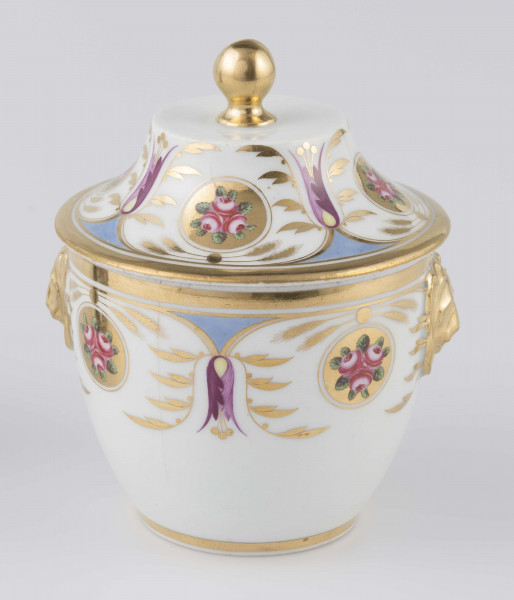 S/CS/1388/2/ML - Cukiernica półowoidalna z uchwytami w formie półplastycznych lwich głów i pokrywką w kształcie ściętego stożka o wklęsłych bokach z kulistym uchwytem. Dekoracja malowana wielobarwnie i złocona: brzusiec i boki pokrywki obiega szeroki fryz złożony ze stylizowanych ornamentów roślinnych (gałązek, kłosów zbóż i liści akantu)  połączonych z owalnymi medalionami, w których są trzy różowe różyczki z zielonymi listkami na złotym tle.Uchwyty malowane złotem,  złotym konturem obwiedzione wszystkie krawędzie.
 