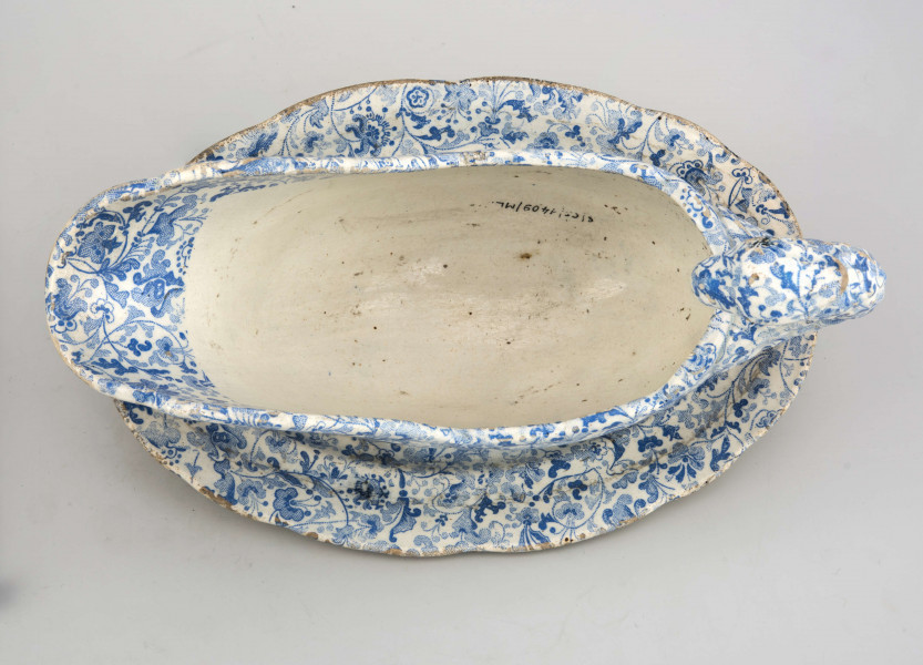 Sosjerka łódkowata z szerokim lekko wywiniętym wylewem, uchwyt wysoki w kształcie plastycznie modelowanej ptasiej głowy; zespolona z podstawką w formie owalnego talerzyka  z profilowanym kołnierzem. Powierzchnia pokryta białą glazurą , na niej niebieski nadruk z wzorem tzw. tapetowym złożonym ze stylizowanych motywów roślinnych. 
 