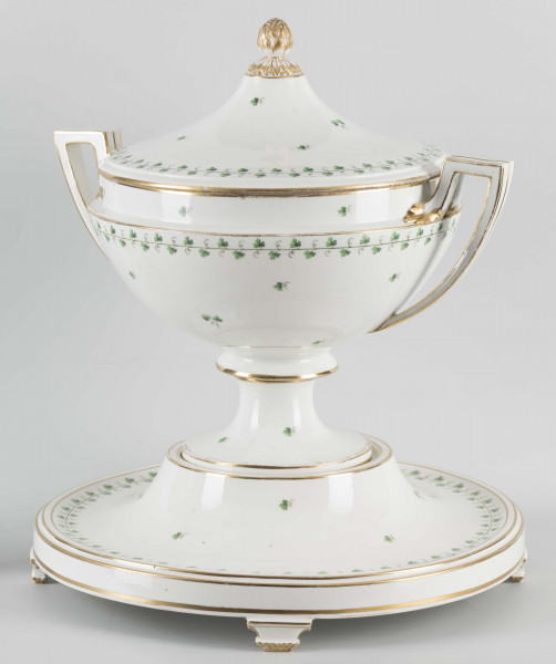 S/CS/1231/ML - Waza półkulista z przewężeniem poniżej wylewu, ucha łamane, stopa o okrągłej podstawie i wąskim trzonie wywiniętym u góry, pokrywa w formie wyniesionego stożka z plastycznym zwieńczeniem i uchwytem w kształcie szyszki. Dekoracja barwnie malowana i złocona: brzusiec, pokrywa i podstawa obwiedzione fryzem winorośli, na powierzchni rytmicznie rozrzucone pojedyncze liski, krawędzie, ucha i uchwyt pokrywy konturowane złotem, 
Podstawa w formie wyniesionego ściętego stożka z okrągłym wgłębieniem u góry, na trzech kostkowych nóżkach. 
 
