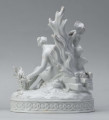 S/CS/1456/ML - Grupa figuralna z białej szkliwionej porcelany. Cokół owalny, wysklepiony z ornamentem opaskowym złożonym ze splecionych owali z rozetkami. Na nim siedzi naga kobieta (Venus) przed płonącym stosem o wysokich płomieniach i wyciągniętą w bok prawą ręką powstrzymuje nagie dziecko (Amorek) zapalające od ognia pochodnię, lewą ręką siega do ażurowego naczynia z ogniem. Za nią na powierzchni cokołu drobne roślinki.
