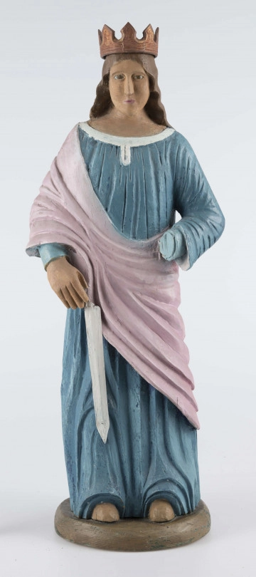 E/16790/ML - Rzeźba drewniana pełna polichromowana, przedstawiająca św. Katarzynę. Postać stojąca, ubrana w niebieską (wcześniej kolor ultramaryny) suknię, żłobioną  w fałdy, z białym wykończeniem przy szyi. Na wierzch, na prawe ramię, narzucony płaszcz/szal w kolorze jasnoróżowym. Prawa ręka opuszczona, trzyma miecz (obecnie samo ostrze koloru białego), lewa zgięta jest w łokciu – brak partii dłoni. Odsłonięte części ciała (stopy, dłonie, szyja, twarz) w kolorze jasnobrązowym; wcześniej prawdopodobnie beżowo-kremowe. Twarz owalna, brązowo-błękitne gałki oczne, usta różowe. Włosy brązowe, spływające fałdami do połowy pleców. Na głowie korona z 8 wierzchołkami, żłobiona, brązowa, uszlachetniona złotą farbą. 
Postać stoi na owalnej podstawie (22 x 19 cm), o wys. 3,5 cm, pomalowanej na brązowo (umbra), wcześniej – w szmaragdowej zieleni.
