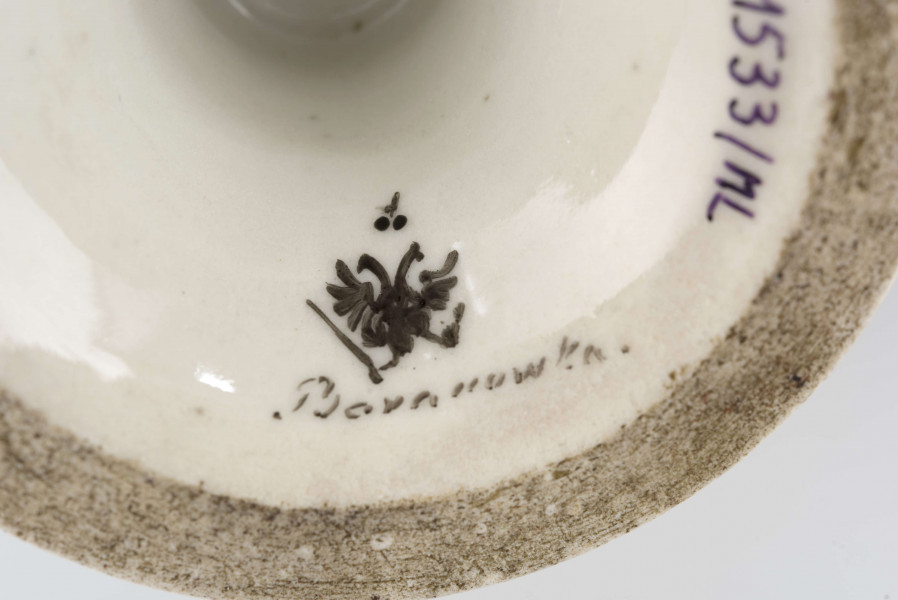 Patera w formie kielicha na okrągłej nóżce, czara w górnej części ażurowa z pionowych pasków zamkniętych ząbkowanym brzegiem. Pokryta białym szkliwem, profile i krawędzie podkreślone paskami w kolorze błękitu kobaltowego.
 