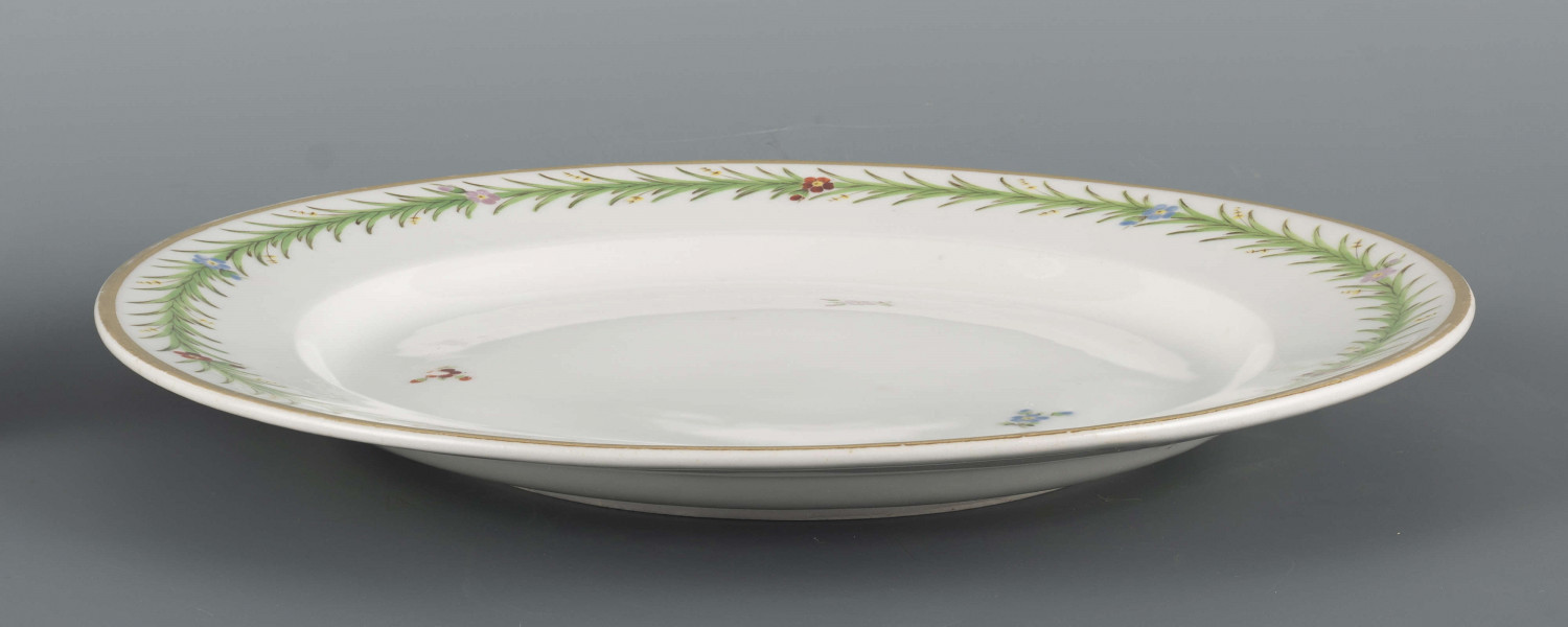 S/CS/1557/ML - Talerz płytki, okrągły, gładki, na kołnierzu malowana zielona  girlanda gęsto uplecionych pędów sitowia, w które wkomponowano pojedyncze kwiatki niezapominajek - niebieskie, czerwone i filoletowe. 
 