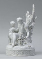 S/CS/1456/ML - Grupa figuralna z białej szkliwionej porcelany. Cokół owalny, wysklepiony z ornamentem opaskowym złożonym ze splecionych owali z rozetkami. Na nim siedzi naga kobieta (Venus) przed płonącym stosem o wysokich płomieniach i wyciągniętą w bok prawą ręką powstrzymuje nagie dziecko (Amorek) zapalające od ognia pochodnię, lewą ręką siega do ażurowego naczynia z ogniem. Za nią na powierzchni cokołu drobne roślinki.
