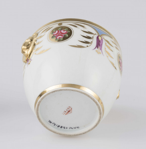 S/CS/1388/2/ML - Cukiernica półowoidalna z uchwytami w formie półplastycznych lwich głów i pokrywką w kształcie ściętego stożka o wklęsłych bokach z kulistym uchwytem. Dekoracja malowana wielobarwnie i złocona: brzusiec i boki pokrywki obiega szeroki fryz złożony ze stylizowanych ornamentów roślinnych (gałązek, kłosów zbóż i liści akantu)  połączonych z owalnymi medalionami, w których są trzy różowe różyczki z zielonymi listkami na złotym tle.Uchwyty malowane złotem,  złotym konturem obwiedzione wszystkie krawędzie.
 