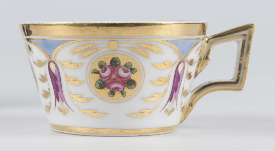 S/CS/1388/3/ML - Filiżanka koniczna, ucho łamane, profilowane, z przewiązkami w osadzeniach.  Dekoracja malowana wielobarwnie i złocona: brzusiec obiega szeroki fryz złożony ze stylizowanych ornamentów roślinnych (gałązek, kłosów zbóż i liści akantu)  połączonych z owalnymi medalionami, w których są trzy różowe różyczki z zielonymi listkami na złotym tle. Wylew złocony, złotym konturem obwiedzione ucho.
 