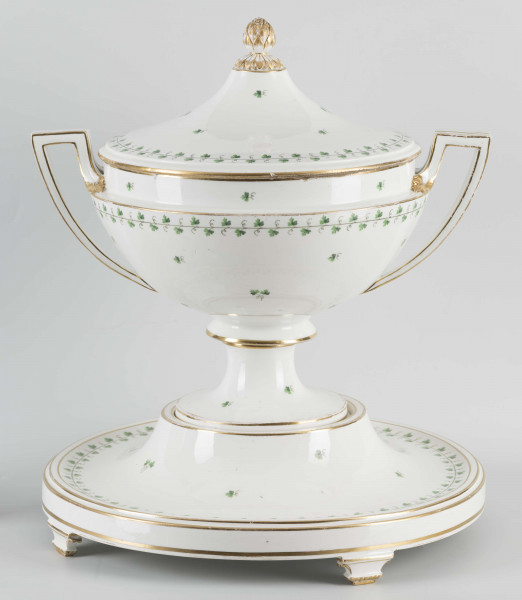 S/CS/1231/ML - Waza półkulista z przewężeniem poniżej wylewu, ucha łamane, stopa o okrągłej podstawie i wąskim trzonie wywiniętym u góry, pokrywa w formie wyniesionego stożka z plastycznym zwieńczeniem i uchwytem w kształcie szyszki. Dekoracja barwnie malowana i złocona: brzusiec, pokrywa i podstawa obwiedzione fryzem winorośli, na powierzchni rytmicznie rozrzucone pojedyncze liski, krawędzie, ucha i uchwyt pokrywy konturowane złotem, 
Podstawa w formie wyniesionego ściętego stożka z okrągłym wgłębieniem u góry, na trzech kostkowych nóżkach. 
 
