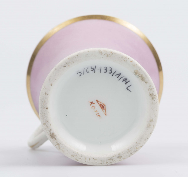 S/CS/133/1/ML - Filiżanka koniczna z rozchylonym wylewem, na niskiej stopie, ucho w formie pastorału z wolutą wyciągnietą ponad krawędź wylewu, zdobioną reliefową rozetką. Powierzchnia matowa malowana w całości na liliowy kolor, wylew obustronnie obwiedziony złotym paskiem, złotym konturem podkreślony brzeg stopy i profile ucha.
