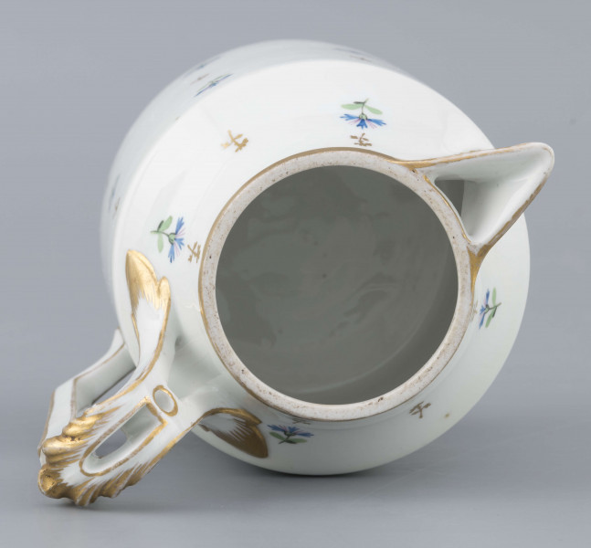 S/CS/1511/ML - Dzbanek cylindryczny, na trzech nóżkach w kształcie lwich łap, szyja w formie zwężonego pierścienia, wylew z dziobkiem, ucho dołem prostokątnie załamane, górą wygięte, rozdwojone, z reliefowymi liśćmi w osadzeniach. Przykrywa w formie wąskiego, konicznego pierścienia, z uchwytem w kształcie szyszki. Dekoracja malowana: regularny rzut drownych chabrów w kolorach błękitu i zieleni. Krawędzie,  ucho, dziobek, nóżki i uchwyt pokrywki konturowane złotem.
