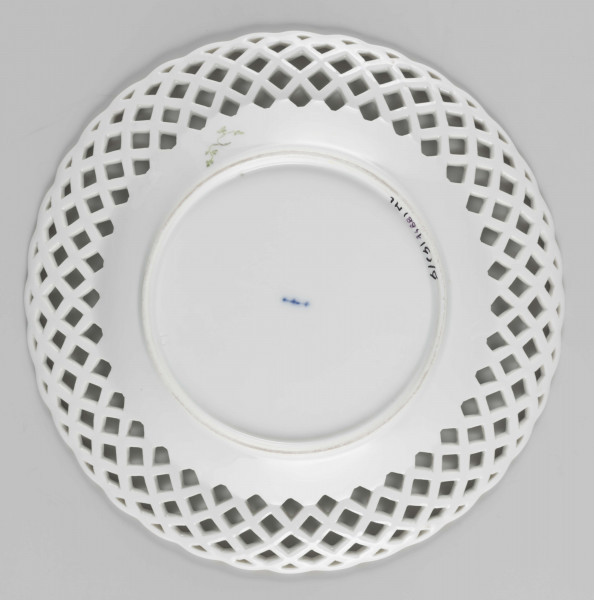 S/CS/1488/ML - Talerz płytki pokryty reliefową plecionką koszykową, w partii kołnierza ażurowo wyciętą. Układ  plecionki  tworzy falistą  linię brzegu. Na dnie malowany wielobarwnie pęk fantazyjnych  kwiatów  i trzy małe kwiatowe gałązki, na spodzie kołnierza zielona gałązka z listkami. 
 