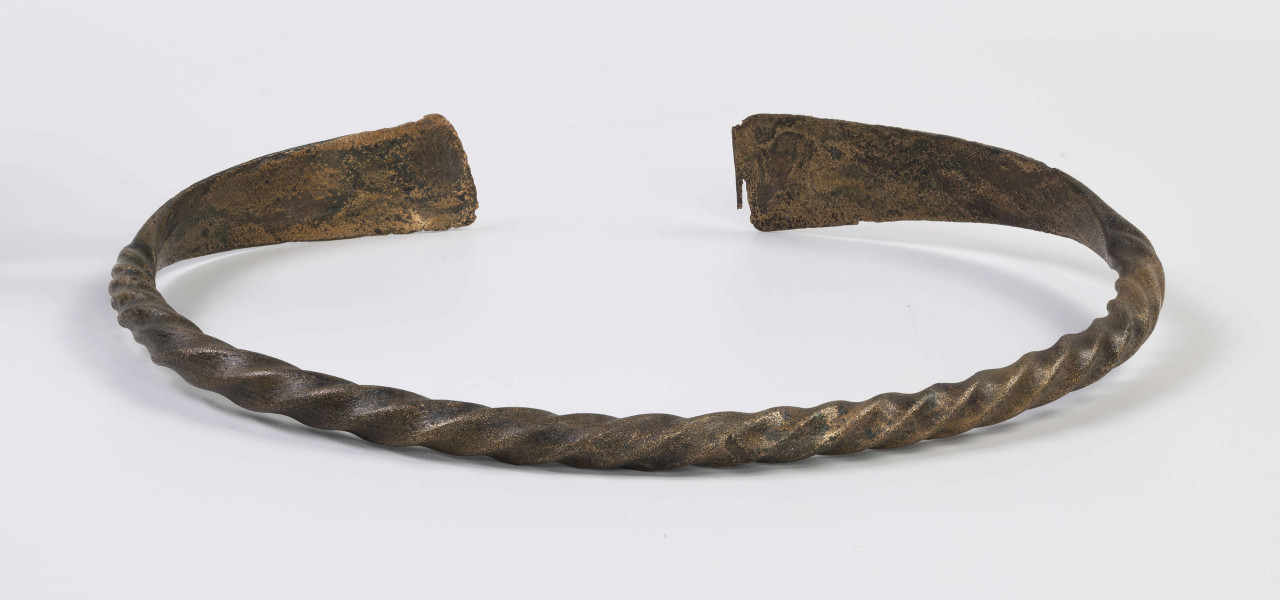 1396/A/ML/4 - Naszyjnik brązowy wykonany z czworograniastego pręta skręconego dookoła swej osi. Oba kóńce naszyjnika spłaszczone i nadkruszone. Naszyjnik bardzo silnie wytarty od dłuższego używania. 