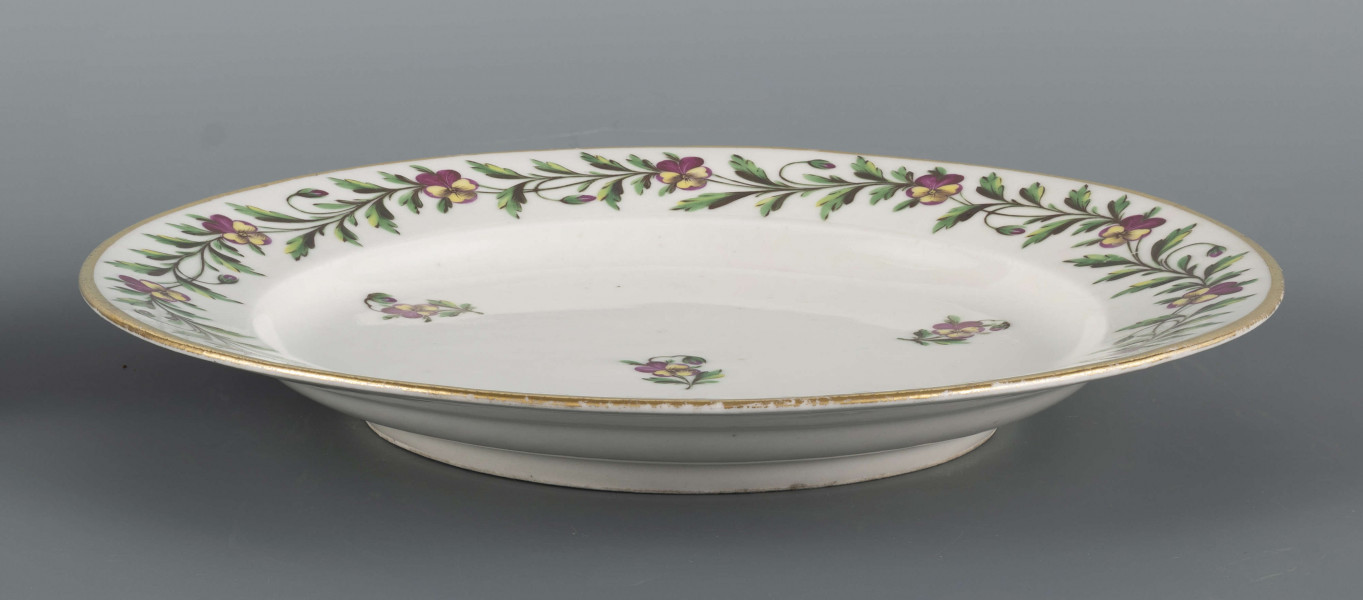 S/CS/1397/ML - Talerz płytki, okrągły, gładki, brzeg konturowany złotem. Kołnierz zdobiony malowaną girlandą bratków trójbarwnych z zielonymi łodyżkami, w lustrze regularnie rozmieszczone 4 pojedyncze kwiatki z listkami.
 