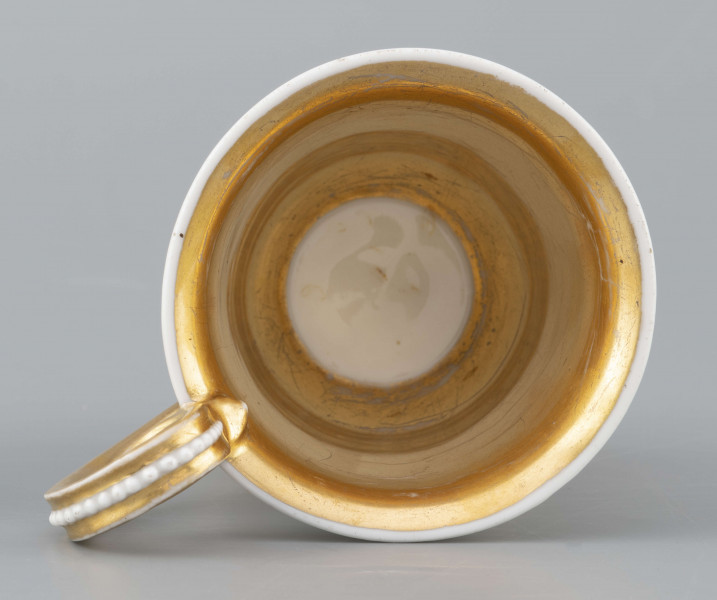 S/CS/1583/ML - Filiżanka koniczna, wylew lekko wywinięty, stopa w kształcie ściętego stożka, ucho wyciągnięte ponad wylew z rozetą  w górnym osadzeniu i wzorem perełek na powierzchni. Dekoracja malowana wielobarwnie: frontalnie na białym tle miniatura ze sceną parkową: od lewej drzewo, para spacerująca wokół gazonu, w głębi daleki pejzaż, na prawo stojąca rzeżba - personifikacja Sprawiedliwości z podpisem na cokole 