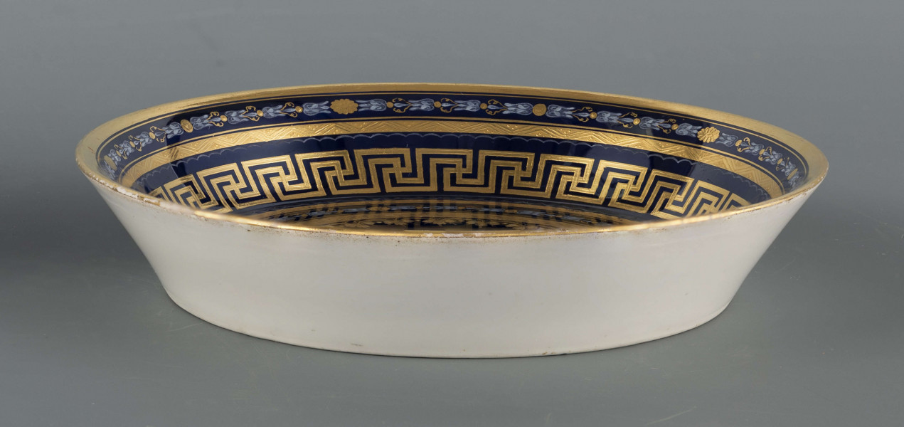 S/CS/1160/ML - Spodek okrągły, konicznie wgłębiony,  na nim bogata dekoracja w wypukłym złocie z ornamentów groteskowych, perełek i wzorów geometrycnych, ułożona w koncentryczne kręgi przedzielone wąskimi paskami jasnej zieleni, z rozetą pośrodku. Na kołnierzu wydzielone 3 migdałowate medaliony, wewnątrz nich mianiatury en grisaille na liliowym tle przedstawiające dwa połączone maszkarony 
  