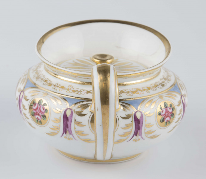 S/CS/1388/1/ML - Brzusiec w formie spłaszczonej kuli, ucho zaokrąglone wyciągnięte ponad górną  krawędź, dziobek lekko wygięty osadzony w dolnej połowie korpusu i uniesiony ku górze. Wokół wylewu wysoki kołnierz ze skośnym ścięciem wyżej uniesionym od strony dziobka, z odchylonymi na zewnątrz ściankami. Pokrywka płaska z uchwytem w postaci płaskiego guzika. Dekoracja malowana wielobarwnie i złocona: brzusiec obiega szeroki fryz złożony ze stylizowanych ornamentów roślinnych (gałązek, kłosów zbóż i liści akantu)  połączonych z owalnymi medalionami, w których są trzy różowe różyczki z zielonymi listkami na złotym tle. Krawędź górną i boki kołnierza obiega ornamentalna złota bordiura, na pokrywce stylizowana złota rozeta, złotym konturem obwiedzione wszystkie krawędzie.
 