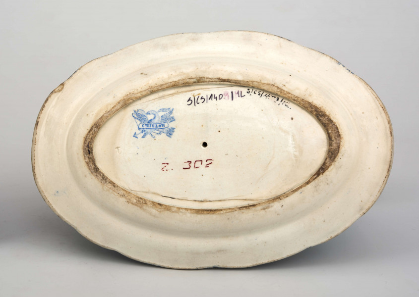 Sosjerka łódkowata z szerokim lekko wywiniętym wylewem, uchwyt wysoki w kształcie plastycznie modelowanej ptasiej głowy; zespolona z podstawką w formie owalnego talerzyka  z profilowanym kołnierzem. Powierzchnia pokryta białą glazurą , na niej niebieski nadruk z wzorem tzw. tapetowym złożonym ze stylizowanych motywów roślinnych. 
 