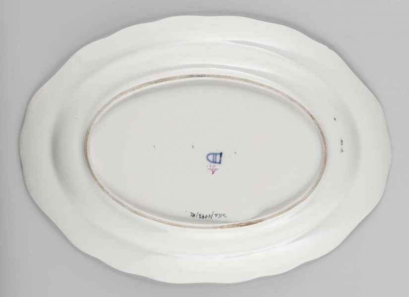 S/CS/1193/ML - Półmisek owalny, wgłębiny, o falistym wykroju brzegu i pogrubionej krawędzi lekko wywiniętej ku górze. Malowany wielobarwnie we wzór kwiatowy: pośrodku lustra duży bukiet z różą, po jego bokach wzduż dłższej osi dwie małe gałązki, na kołnierzu regularnie romieszczonych 6 gałązek kwiatowych. Barwy: róż, fiolet, żółcień ,czerwień, błękit , dwa odcienie zieleni. 
