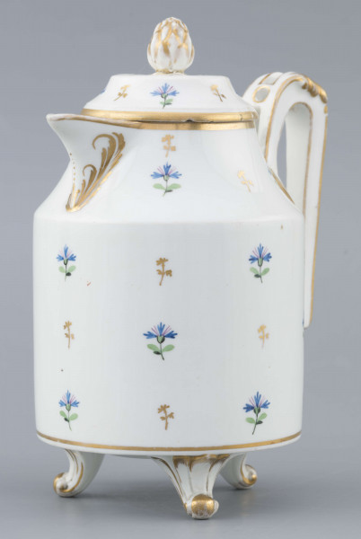 S/CS/1511/ML - Dzbanek cylindryczny, na trzech nóżkach w kształcie lwich łap, szyja w formie zwężonego pierścienia, wylew z dziobkiem, ucho dołem prostokątnie załamane, górą wygięte, rozdwojone, z reliefowymi liśćmi w osadzeniach. Przykrywa w formie wąskiego, konicznego pierścienia, z uchwytem w kształcie szyszki. Dekoracja malowana: regularny rzut drownych chabrów w kolorach błękitu i zieleni. Krawędzie,  ucho, dziobek, nóżki i uchwyt pokrywki konturowane złotem.
