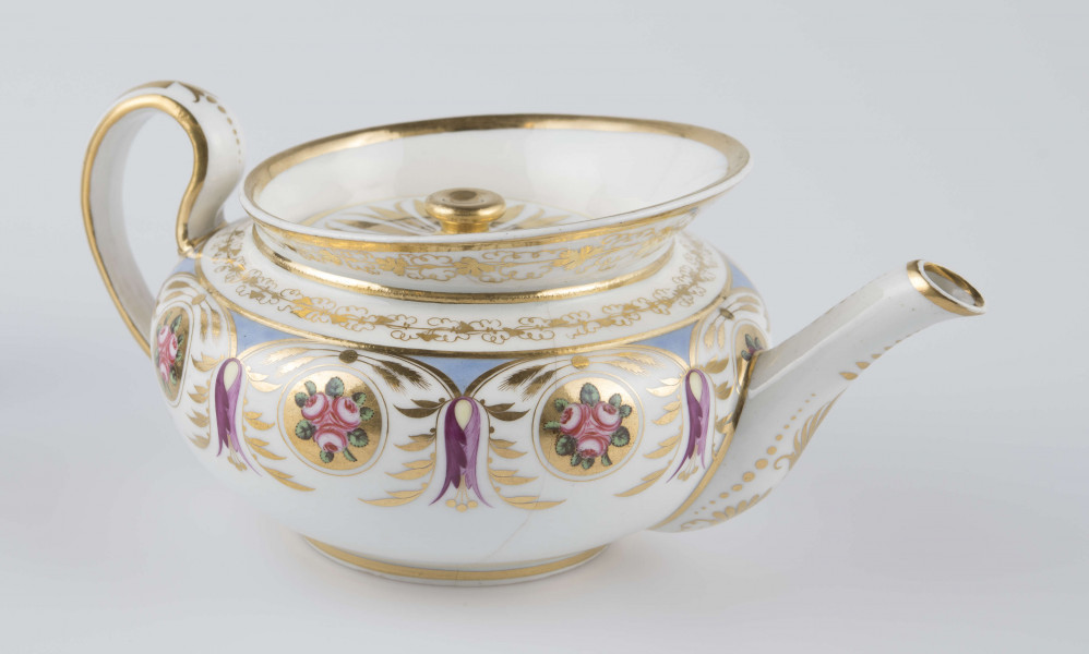 S/CS/1388/1/ML - Brzusiec w formie spłaszczonej kuli, ucho zaokrąglone wyciągnięte ponad górną  krawędź, dziobek lekko wygięty osadzony w dolnej połowie korpusu i uniesiony ku górze. Wokół wylewu wysoki kołnierz ze skośnym ścięciem wyżej uniesionym od strony dziobka, z odchylonymi na zewnątrz ściankami. Pokrywka płaska z uchwytem w postaci płaskiego guzika. Dekoracja malowana wielobarwnie i złocona: brzusiec obiega szeroki fryz złożony ze stylizowanych ornamentów roślinnych (gałązek, kłosów zbóż i liści akantu)  połączonych z owalnymi medalionami, w których są trzy różowe różyczki z zielonymi listkami na złotym tle. Krawędź górną i boki kołnierza obiega ornamentalna złota bordiura, na pokrywce stylizowana złota rozeta, złotym konturem obwiedzione wszystkie krawędzie.
 