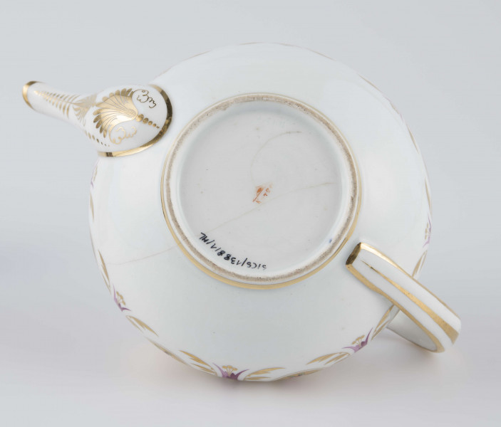 S/CS/1388/1/ML - Brzusiec w formie spłaszczonej kuli, ucho zaokrąglone wyciągnięte ponad górną  krawędź, dziobek lekko wygięty osadzony w dolnej połowie korpusu i uniesiony ku górze. Wokół wylewu wysoki kołnierz ze skośnym ścięciem wyżej uniesionym od strony dziobka, z odchylonymi na zewnątrz ściankami. Pokrywka płaska z uchwytem w postaci płaskiego guzika. Dekoracja malowana wielobarwnie i złocona: brzusiec obiega szeroki fryz złożony ze stylizowanych ornamentów roślinnych (gałązek, kłosów zbóż i liści akantu)  połączonych z owalnymi medalionami, w których są trzy różowe różyczki z zielonymi listkami na złotym tle. Krawędź górną i boki kołnierza obiega ornamentalna złota bordiura, na pokrywce stylizowana złota rozeta, złotym konturem obwiedzione wszystkie krawędzie.
 