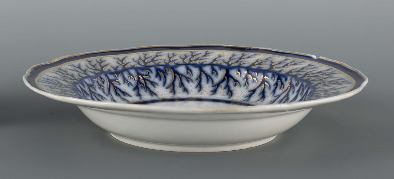 S/CS/1401/ML - Talerz głęboki, okrągły, z wodrębnioną fasetą, brzeg kołnierza falisty. Zdobiony malowanym wzorem kobaltowym i złoceniem: na kołnierzu i fasecie nieulistnione gałązki stylizowanej tarniny konturowane złotem, w tle złota siateczka, ujęte w szerokie kobaltowe obwódki. 
 
