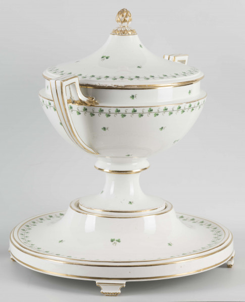 S/CS/1231/ML - Waza półkulista z przewężeniem poniżej wylewu, ucha łamane, stopa o okrągłej podstawie i wąskim trzonie wywiniętym u góry, pokrywa w formie wyniesionego stożka z plastycznym zwieńczeniem i uchwytem w kształcie szyszki. Dekoracja barwnie malowana i złocona: brzusiec, pokrywa i podstawa obwiedzione fryzem winorośli, na powierzchni rytmicznie rozrzucone pojedyncze liski, krawędzie, ucha i uchwyt pokrywy konturowane złotem, 
Podstawa w formie wyniesionego ściętego stożka z okrągłym wgłębieniem u góry, na trzech kostkowych nóżkach. 
 
