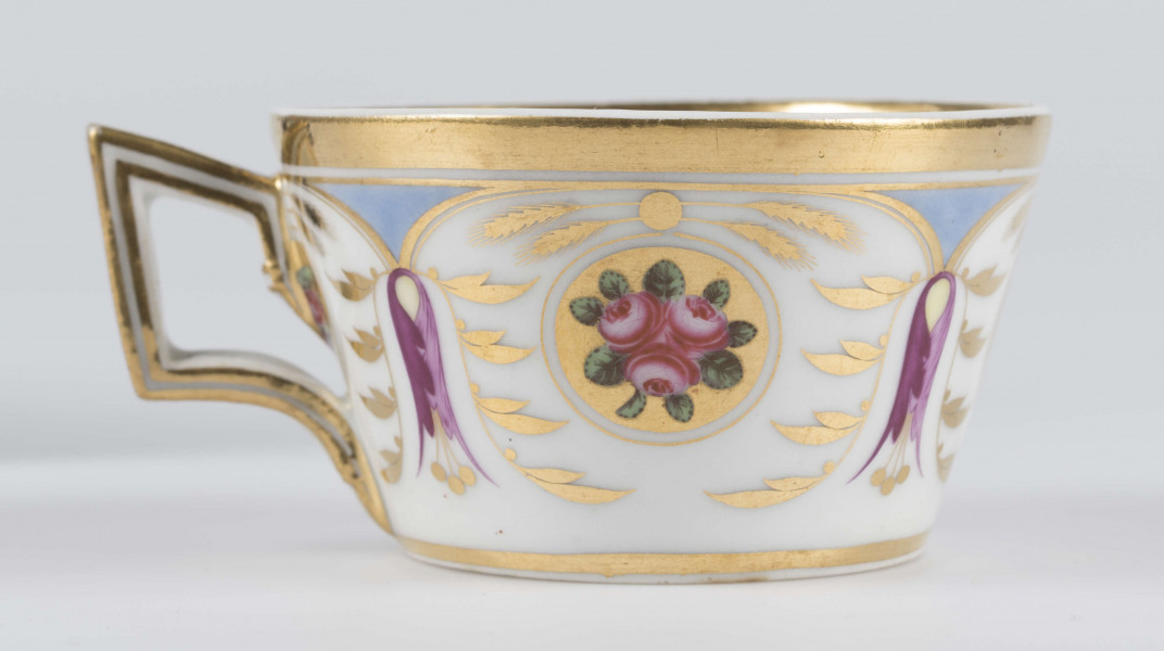 S/CS/1388/3/ML - Filiżanka koniczna, ucho łamane, profilowane, z przewiązkami w osadzeniach.  Dekoracja malowana wielobarwnie i złocona: brzusiec obiega szeroki fryz złożony ze stylizowanych ornamentów roślinnych (gałązek, kłosów zbóż i liści akantu)  połączonych z owalnymi medalionami, w których są trzy różowe różyczki z zielonymi listkami na złotym tle. Wylew złocony, złotym konturem obwiedzione ucho.
 