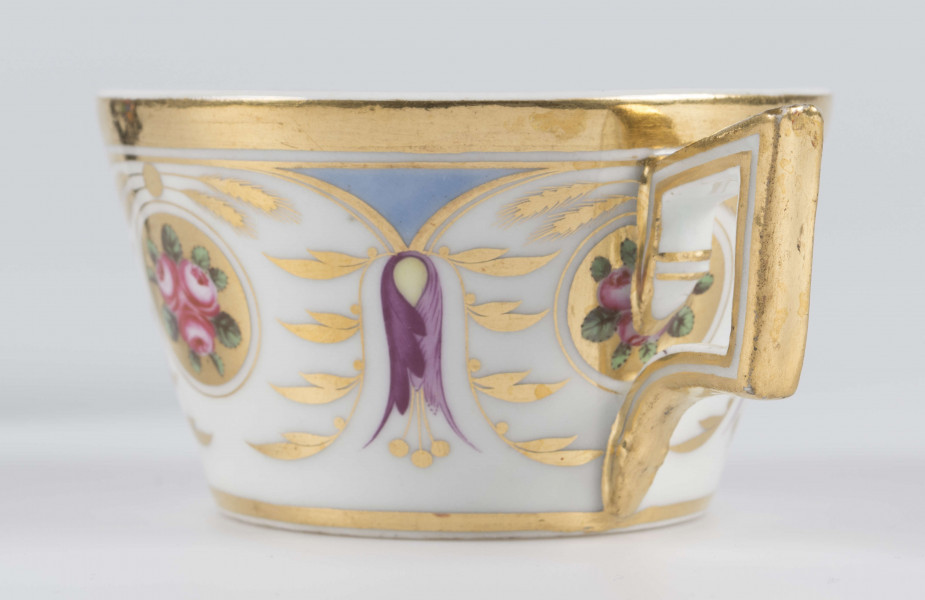 S/CS/1388/3/ML - Filiżanka koniczna, ucho łamane, profilowane, z przewiązkami w osadzeniach.  Dekoracja malowana wielobarwnie i złocona: brzusiec obiega szeroki fryz złożony ze stylizowanych ornamentów roślinnych (gałązek, kłosów zbóż i liści akantu)  połączonych z owalnymi medalionami, w których są trzy różowe różyczki z zielonymi listkami na złotym tle. Wylew złocony, złotym konturem obwiedzione ucho.
 