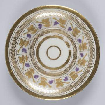S/CS/136/2/ML - Spodek koniczny z wywiniętym kołnierzem, na pierścieniowej podstawie, wgłębiony. Dekoracja malowana złotem z dodatkiem fioletowej purpury:  na kołnierzu wykreślony złotem ciąg kwadratów wypełnionych motywem winogrona na złotej gałązce, obramowana wicią złotych listków, dolna i górna krawędź obwiedzione złotymi paskami, 
