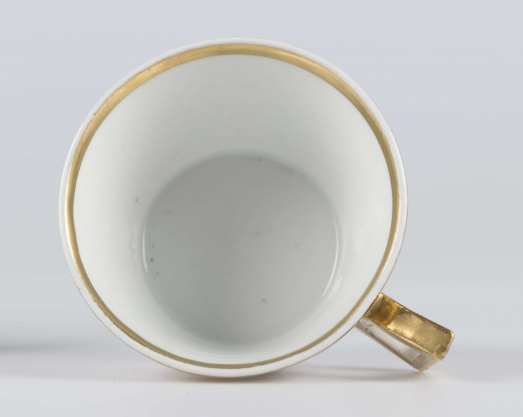 S/CS/1388/3/ML - Filiżanka koniczna, ucho łamane, profilowane, z przewiązkami w osadzeniach.  Dekoracja malowana wielobarwnie i złocona: brzusiec obiega szeroki fryz złożony ze stylizowanych ornamentów roślinnych (gałązek, kłosów zbóż i liści akantu)  połączonych z owalnymi medalionami, w których są trzy różowe różyczki z zielonymi listkami na złotym tle. Wylew złocony, złotym konturem obwiedzione ucho.
 