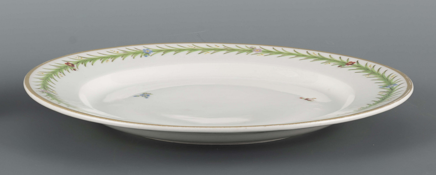 S/CS/1557/ML - Talerz płytki, okrągły, gładki, na kołnierzu malowana zielona  girlanda gęsto uplecionych pędów sitowia, w które wkomponowano pojedyncze kwiatki niezapominajek - niebieskie, czerwone i filoletowe. 
 