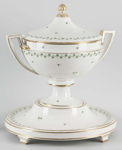 S/CS/1231/ML - Waza półkulista z przewężeniem poniżej wylewu, ucha łamane, stopa o okrągłej podstawie i wąskim trzonie wywiniętym u góry, pokrywa w formie wyniesionego stożka z plastycznym zwieńczeniem i uchwytem w kształcie szyszki. Dekoracja barwnie malowana i złocona: brzusiec, pokrywa i podstawa obwiedzione fryzem winorośli, na powierzchni rytmicznie rozrzucone pojedyncze liski, krawędzie, ucha i uchwyt pokrywy konturowane złotem, 
Podstawa w formie wyniesionego ściętego stożka z okrągłym wgłębieniem u góry, na trzech kostkowych nóżkach. 
 
