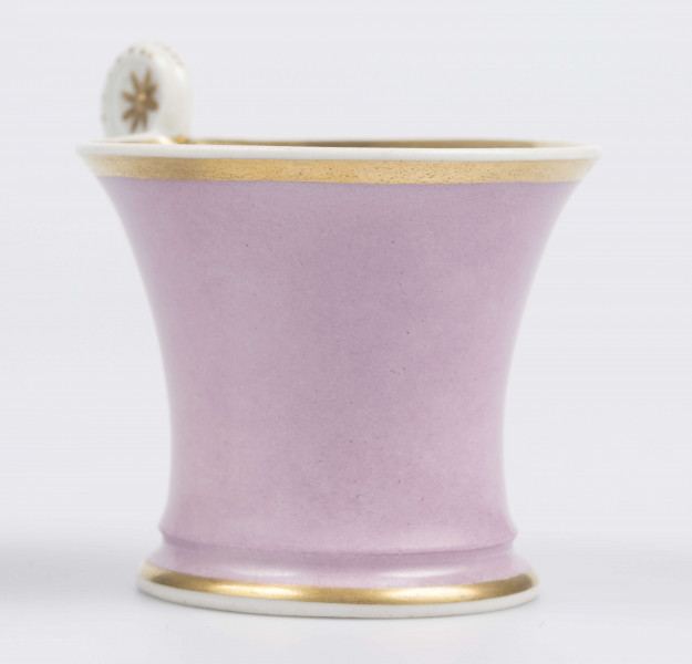 S/CS/133/1/ML - Filiżanka koniczna z rozchylonym wylewem, na niskiej stopie, ucho w formie pastorału z wolutą wyciągnietą ponad krawędź wylewu, zdobioną reliefową rozetką. Powierzchnia matowa malowana w całości na liliowy kolor, wylew obustronnie obwiedziony złotym paskiem, złotym konturem podkreślony brzeg stopy i profile ucha.
