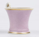 S/CS/133/1/ML - Filiżanka koniczna z rozchylonym wylewem, na niskiej stopie, ucho w formie pastorału z wolutą wyciągnietą ponad krawędź wylewu, zdobioną reliefową rozetką. Powierzchnia matowa malowana w całości na liliowy kolor, wylew obustronnie obwiedziony złotym paskiem, złotym konturem podkreślony brzeg stopy i profile ucha.

