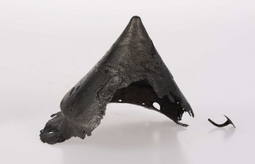 Umbo żelazne, stożkowate z zachowanym jednym płaskim nitem w brzegu. Stożek łagodnie zakończony.