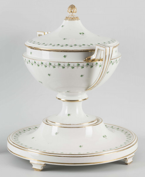 S/CS/1231/ML - Waza półkulista z przewężeniem poniżej wylewu, ucha łamane, stopa o okrągłej podstawie i wąskim trzonie wywiniętym u góry, pokrywa w formie wyniesionego stożka z plastycznym zwieńczeniem i uchwytem w kształcie szyszki. Dekoracja barwnie malowana i złocona: brzusiec, pokrywa i podstawa obwiedzione fryzem winorośli, na powierzchni rytmicznie rozrzucone pojedyncze liski, krawędzie, ucha i uchwyt pokrywy konturowane złotem, 
Podstawa w formie wyniesionego ściętego stożka z okrągłym wgłębieniem u góry, na trzech kostkowych nóżkach. 
 
