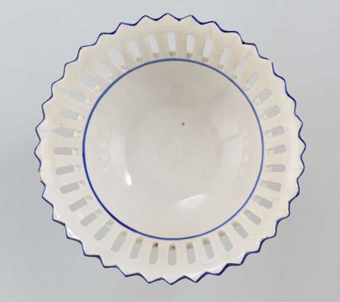 Patera w formie kielicha na okrągłej nóżce, czara w górnej części ażurowa z pionowych pasków zamkniętych ząbkowanym brzegiem. Pokryta białym szkliwem, profile i krawędzie podkreślone paskami w kolorze błękitu kobaltowego.
 