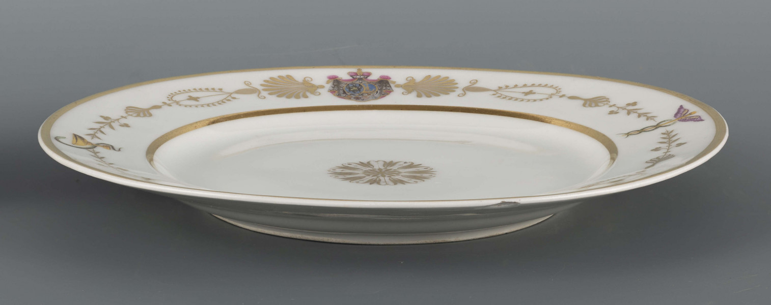 S/CS/1594/ML - Talerz płytki, okrągły, gładki. Na kołnierzu fryz z ornamentu palmetowego przeplecionego barwnymi elementami: kaduceuszem, wężem Eskulapa, monogramem 