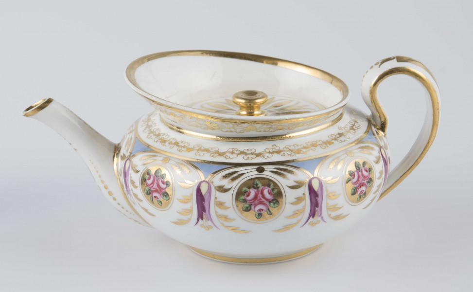 S/CS/1388/1/ML - Brzusiec w formie spłaszczonej kuli, ucho zaokrąglone wyciągnięte ponad górną  krawędź, dziobek lekko wygięty osadzony w dolnej połowie korpusu i uniesiony ku górze. Wokół wylewu wysoki kołnierz ze skośnym ścięciem wyżej uniesionym od strony dziobka, z odchylonymi na zewnątrz ściankami. Pokrywka płaska z uchwytem w postaci płaskiego guzika. Dekoracja malowana wielobarwnie i złocona: brzusiec obiega szeroki fryz złożony ze stylizowanych ornamentów roślinnych (gałązek, kłosów zbóż i liści akantu)  połączonych z owalnymi medalionami, w których są trzy różowe różyczki z zielonymi listkami na złotym tle. Krawędź górną i boki kołnierza obiega ornamentalna złota bordiura, na pokrywce stylizowana złota rozeta, złotym konturem obwiedzione wszystkie krawędzie.
 