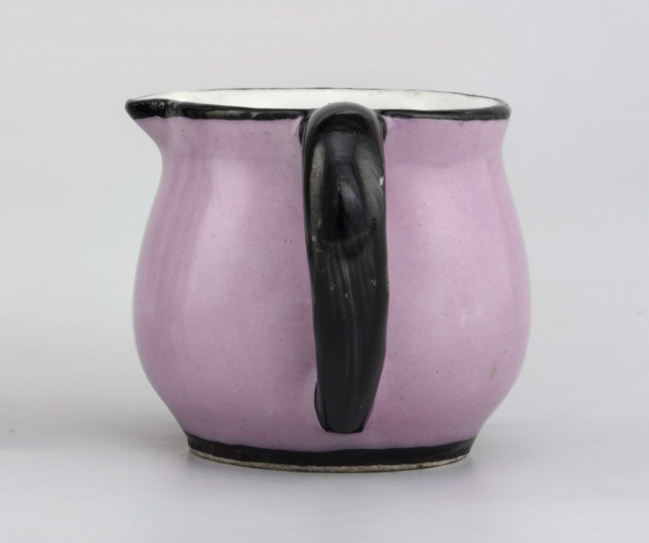 Dzbanuszek w formie spłaszczonej kuli na pierścieniowej stopie, ucho zaokrąglone, wylew lekko wywinięty z małym dziobkiem uformowanym prostopadle do ucha. Powierzchnia malowana  jednolicie  w kolorze jasnego różu, ucho, wylew i stopa malowane na czarno.
 