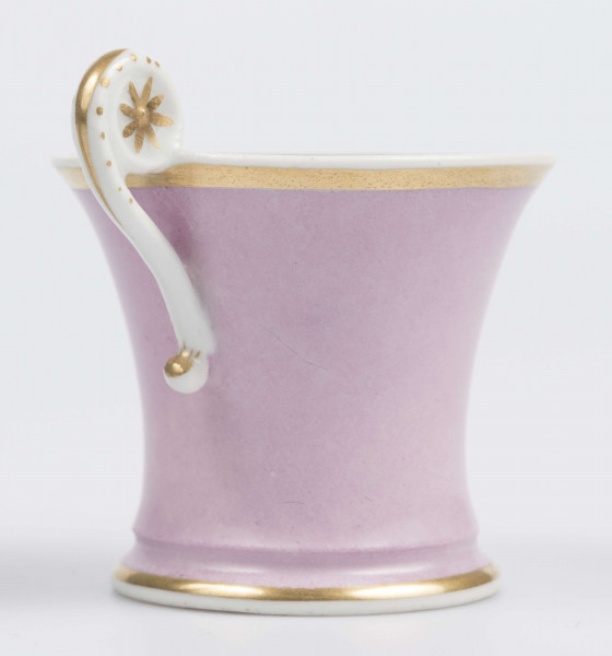 S/CS/133/1/ML - Filiżanka koniczna z rozchylonym wylewem, na niskiej stopie, ucho w formie pastorału z wolutą wyciągnietą ponad krawędź wylewu, zdobioną reliefową rozetką. Powierzchnia matowa malowana w całości na liliowy kolor, wylew obustronnie obwiedziony złotym paskiem, złotym konturem podkreślony brzeg stopy i profile ucha.
