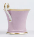 S/CS/133/1/ML - Filiżanka koniczna z rozchylonym wylewem, na niskiej stopie, ucho w formie pastorału z wolutą wyciągnietą ponad krawędź wylewu, zdobioną reliefową rozetką. Powierzchnia matowa malowana w całości na liliowy kolor, wylew obustronnie obwiedziony złotym paskiem, złotym konturem podkreślony brzeg stopy i profile ucha.
