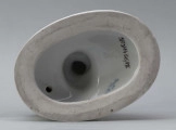 S/CS/1456/ML - Grupa figuralna z białej szkliwionej porcelany. Cokół owalny, wysklepiony z ornamentem opaskowym złożonym ze splecionych owali z rozetkami. Na nim siedzi naga kobieta (Venus) przed płonącym stosem o wysokich płomieniach i wyciągniętą w bok prawą ręką powstrzymuje nagie dziecko (Amorek) zapalające od ognia pochodnię, lewą ręką siega do ażurowego naczynia z ogniem. Za nią na powierzchni cokołu drobne roślinki.

