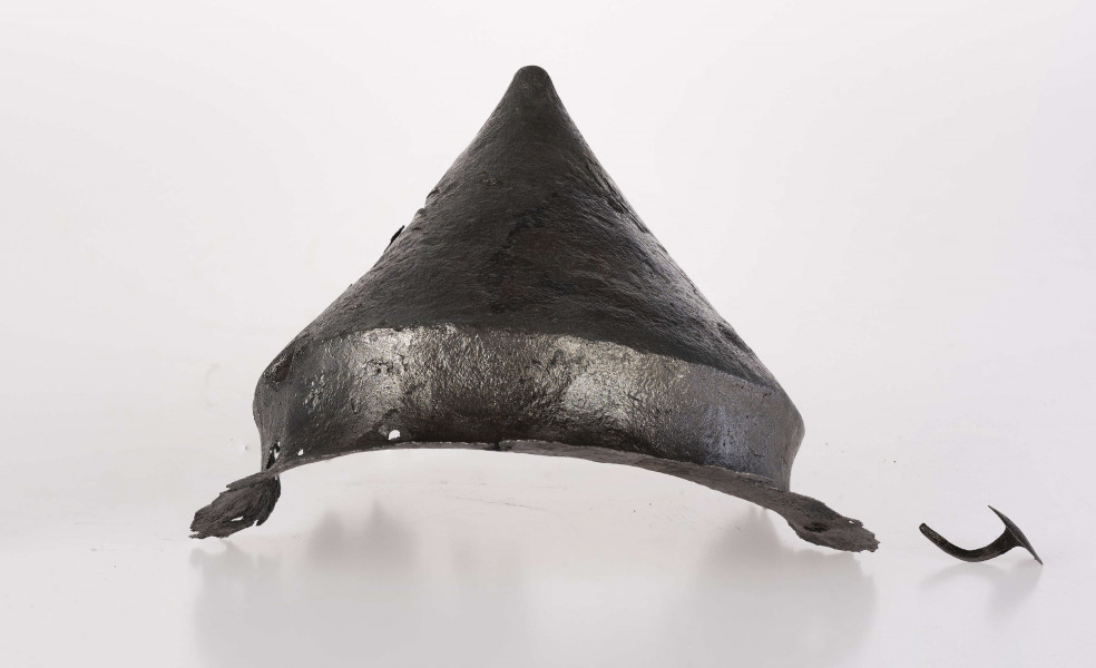 Umbo żelazne, stożkowate z zachowanym jednym płaskim nitem w brzegu. Stożek łagodnie zakończony.