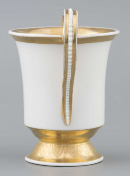 S/CS/1583/ML - Filiżanka koniczna, wylew lekko wywinięty, stopa w kształcie ściętego stożka, ucho wyciągnięte ponad wylew z rozetą  w górnym osadzeniu i wzorem perełek na powierzchni. Dekoracja malowana wielobarwnie: frontalnie na białym tle miniatura ze sceną parkową: od lewej drzewo, para spacerująca wokół gazonu, w głębi daleki pejzaż, na prawo stojąca rzeżba - personifikacja Sprawiedliwości z podpisem na cokole 