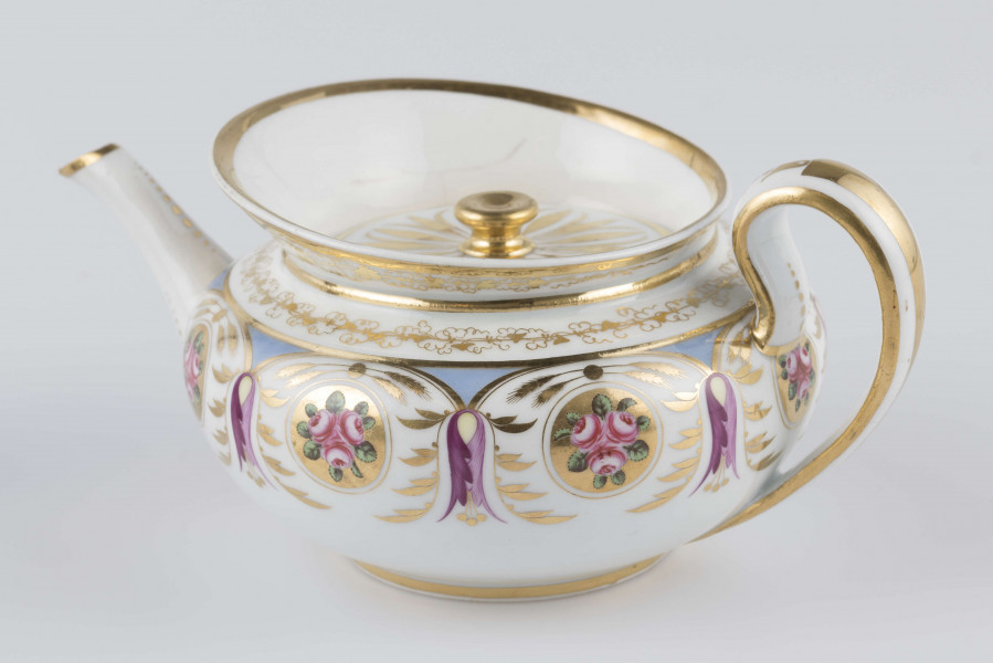 S/CS/1388/1/ML - Brzusiec w formie spłaszczonej kuli, ucho zaokrąglone wyciągnięte ponad górną  krawędź, dziobek lekko wygięty osadzony w dolnej połowie korpusu i uniesiony ku górze. Wokół wylewu wysoki kołnierz ze skośnym ścięciem wyżej uniesionym od strony dziobka, z odchylonymi na zewnątrz ściankami. Pokrywka płaska z uchwytem w postaci płaskiego guzika. Dekoracja malowana wielobarwnie i złocona: brzusiec obiega szeroki fryz złożony ze stylizowanych ornamentów roślinnych (gałązek, kłosów zbóż i liści akantu)  połączonych z owalnymi medalionami, w których są trzy różowe różyczki z zielonymi listkami na złotym tle. Krawędź górną i boki kołnierza obiega ornamentalna złota bordiura, na pokrywce stylizowana złota rozeta, złotym konturem obwiedzione wszystkie krawędzie.
 