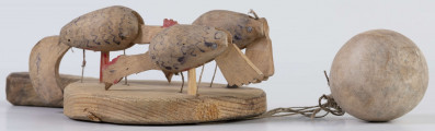 E/17030/ML - Zabawka drewniana przedstawiająca trzy kurki przymocowane do owalnej deseczki z uchwytem. Kurki mają ruchome głowy i ogony, które poruszają się za pomocą sznurków przeciągniętych przez deseczkę i przywiązanych do drewnianej kuli. Deseczka wykonana z drewna sosnowego, kurki z drewna lipowego. Głowy i nogi kurek pomalowane są czerwoną farbą, tułowia zdobi ornament geometryczny w postaci zygzakowatych linii wykonanych brązową farbą.