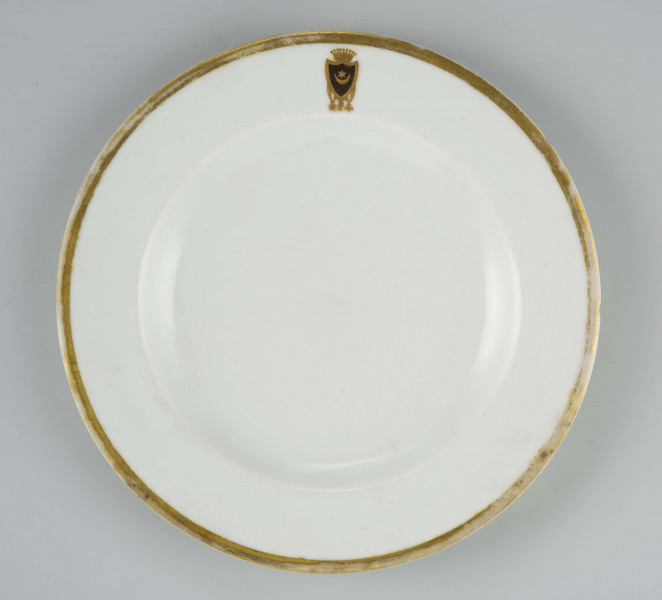 Talerz płytki, okrągły, gładki, brzeg obwiedziony szerokim złotym paskiem, na kołnierzu malowany herb 