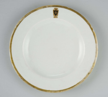 Talerz płytki, okrągły, gładki, brzeg obwiedziony szerokim złotym paskiem, na kołnierzu malowany herb 